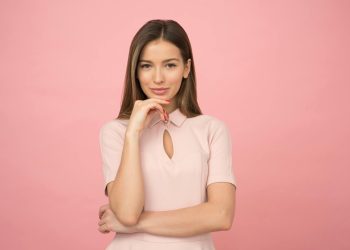Portrait of a young woman posing elegantly in a studio with a pink background.