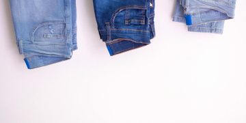 Three pairs of denim jeans neatly folded and hanging against a white backdrop.