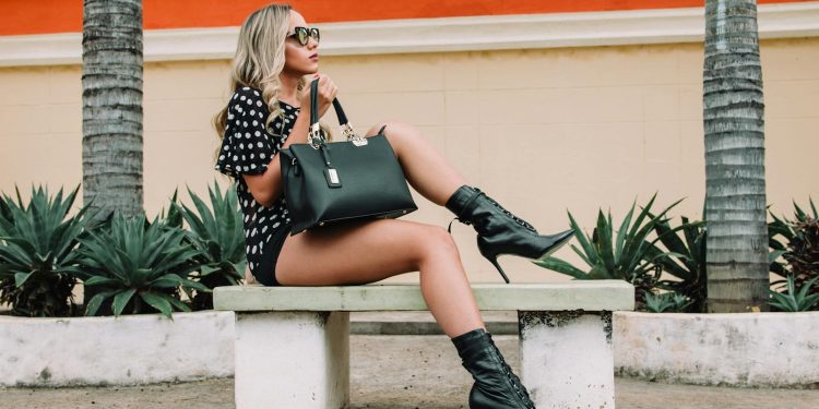 Fashionable woman in boots and sunglasses poses on a bench outdoors.