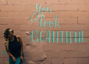 A stylish woman with curly hair and sunglasses poses beside a vibrant mural in Toronto.