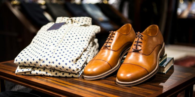Elegant brown leather shoes and printed shirt displayed on a wooden table in a stylish clothing store.