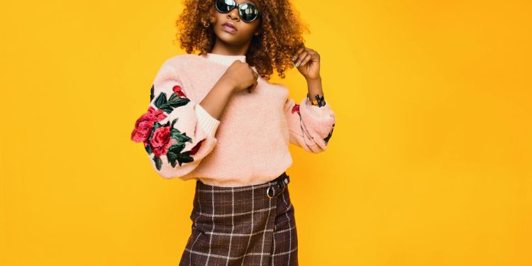 Chic woman with afro hair in a floral sweater and plaid skirt posing confidently.
