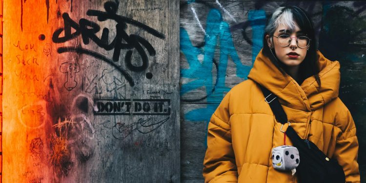 Young woman in yellow winter jacket against vibrant graffiti wall, conveying urban street style.