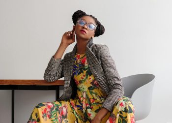 Elegant woman posing in a modern setting, wearing a floral dress and eyeglasses.