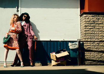 Fashionable duo striking poses against an urban background in stylish outfits.