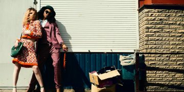 Fashionable duo striking poses against an urban background in stylish outfits.