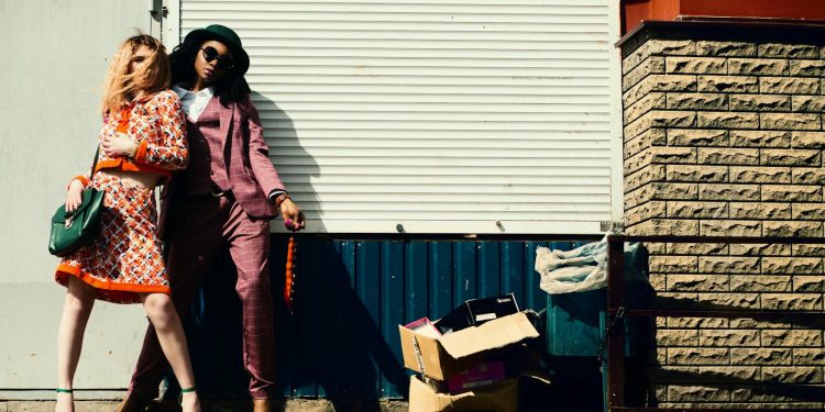 Fashionable duo striking poses against an urban background in stylish outfits.